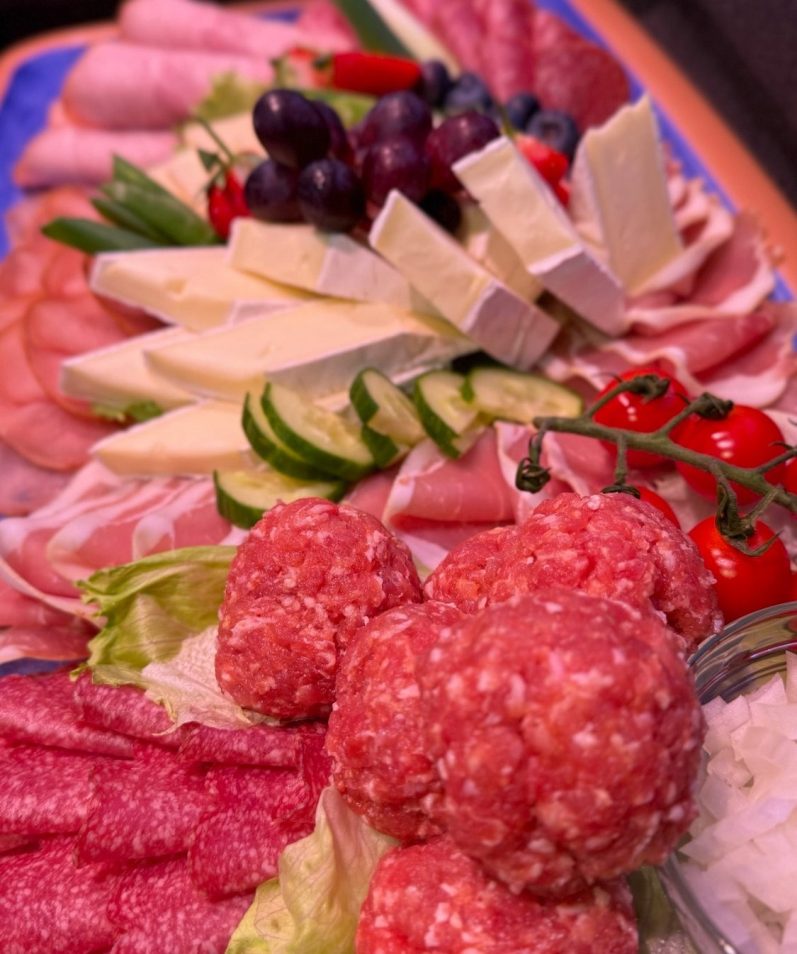 Bunte Platte mit verschiedenen Käsesorten, Wurst, Trauben und frischem Gemüse.