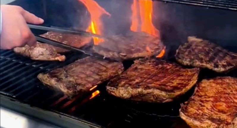 Gegrillte Steaks auf einem Grill, mit einer Hand, die sie wendet.