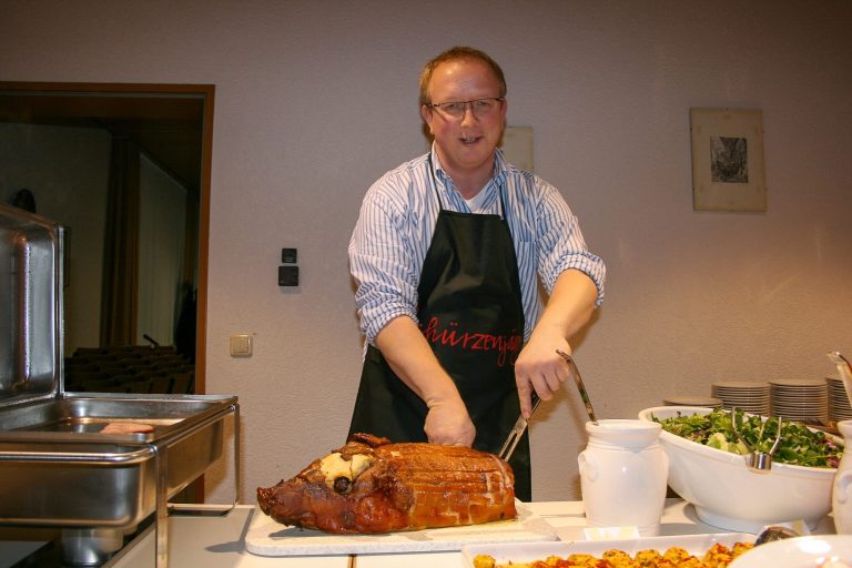 Mann im schwarzen Schürze schneidet ein großes, gebratenes Stück Fleisch.