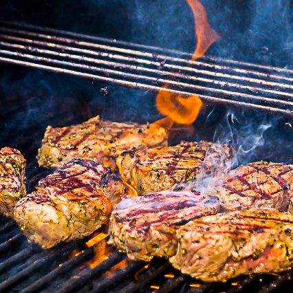 Gegrillte Steaks mit Grillspuren und Flammen, umgeben von Rauch.