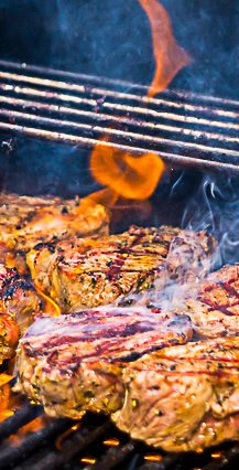 Gegrillte Steaks mit Grillstreifen und aufsteigendem Rauch und Flammen.