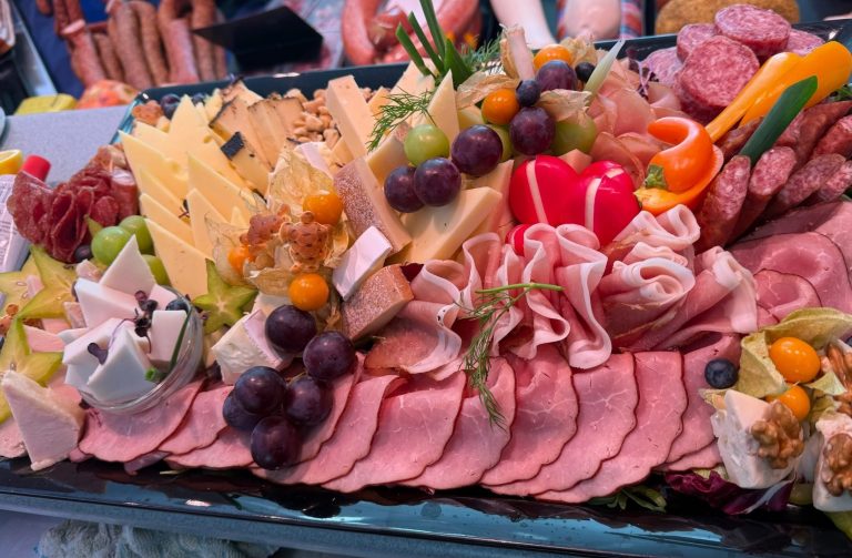 Platte mit verschiedenen Käsesorten, Wurst, Obst und Gemüse dekoriert.