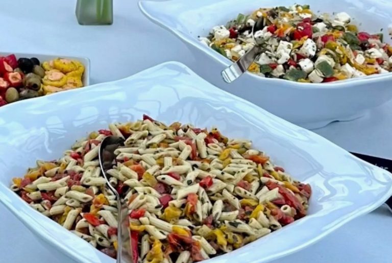 Bunte Pasta-Salate mit Gemüse in großen Schalen auf einem Tisch.