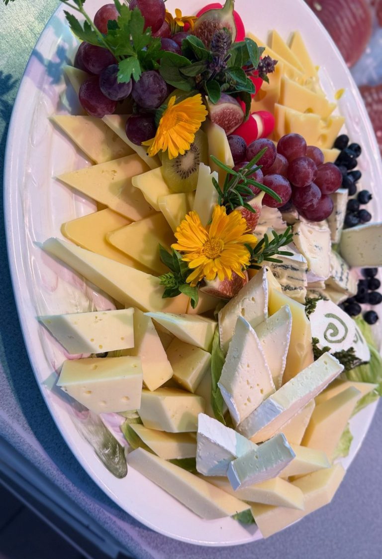 Ein Käsebrett mit verschiedenen Käsesorten, Trauben, Kirschen und essbaren Blumen.