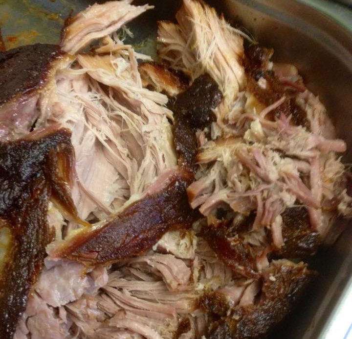 Zerfleddertes Pulled Pork in einer Edelstahlplatte, saftig und goldbraun.