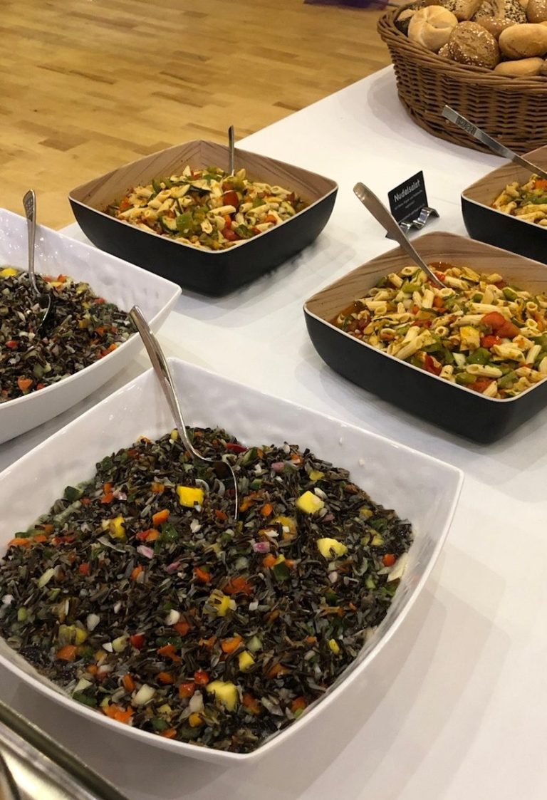 Diverse Salate in Schalen, darunter Linsen- und Gemüsemischung, neben Brotkorb.