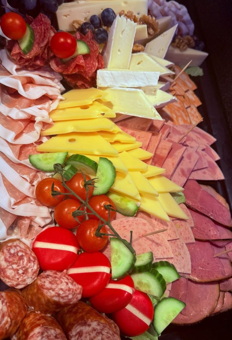 Eine Auswahl an Wurst, Käse, Trauben, Tomaten und Gurkenscheiben auf einem Tablett.